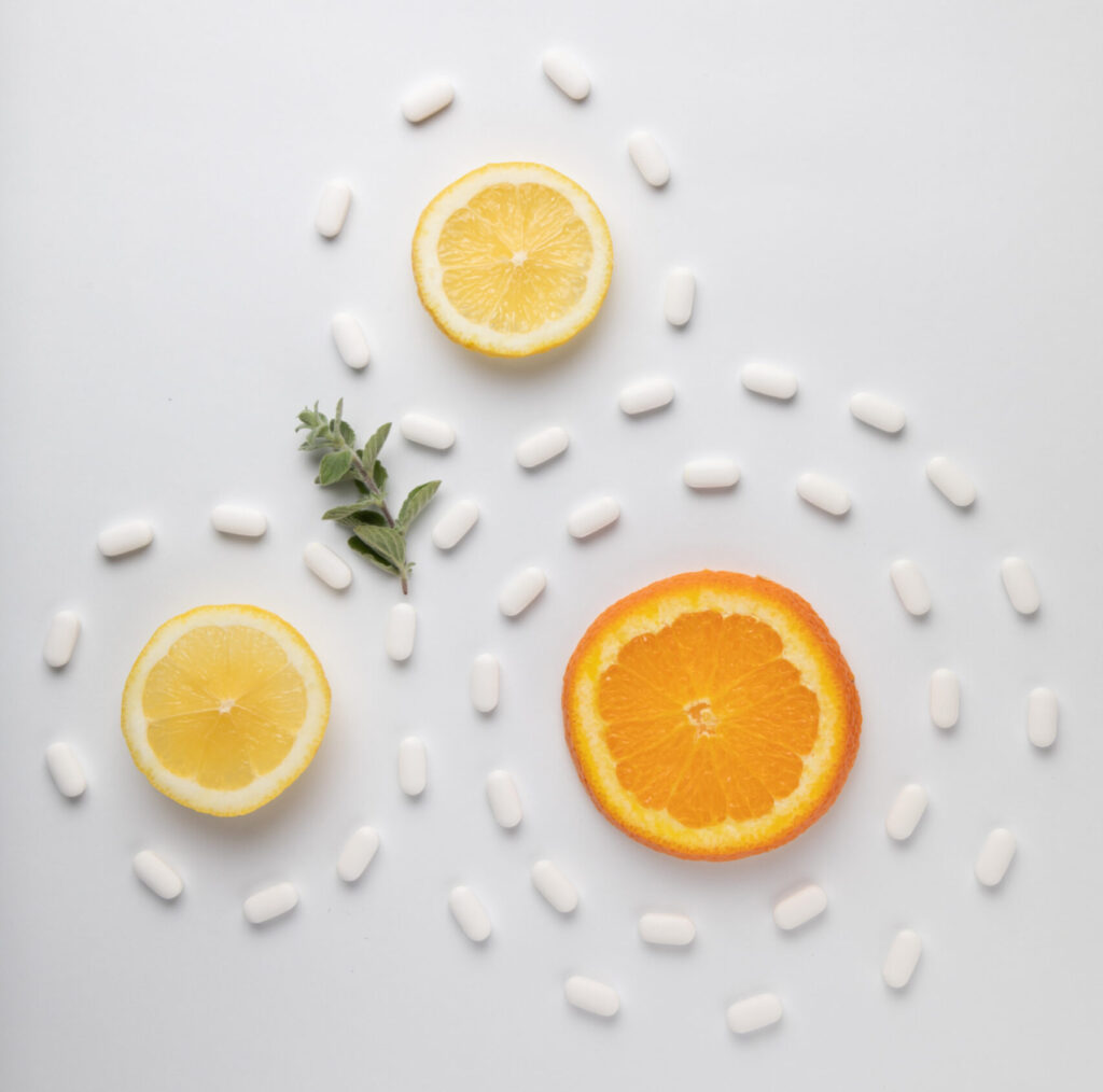 Meia laranja e 2 meios limões, com comprimidos brancos em volta em alusão à vitamina C